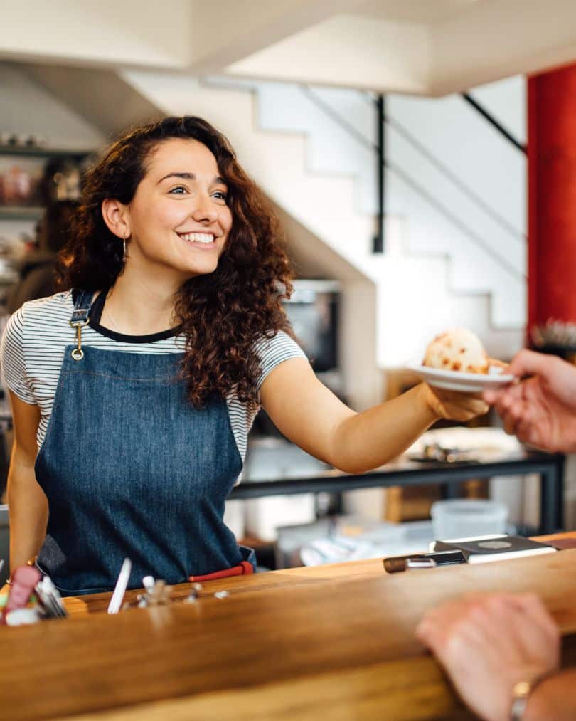 A barista passing a pastry over the counter to a client.