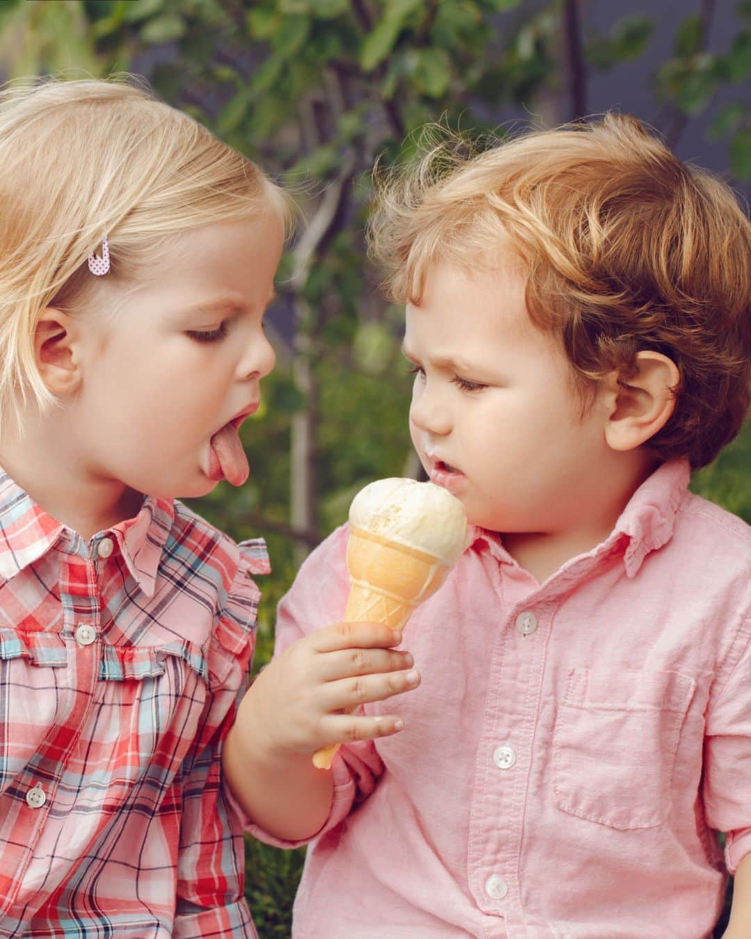 A child trying to lick another child's ice cream.